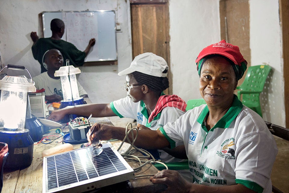  With assistance from UN Women, Musu Junius and Marie Weeks attended Barefoot College solar engineer training in India and have used new skills to electrify their community in Liberia. Behind them, a teacher prepares for evening adult literacy classes made possible by switching on the lights.    Photo: Thomas Dworzak/Magnum Photos for UN Women