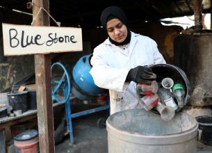 Rawan empties used glass into a barrel to begin the recycling process in Tulkarem village