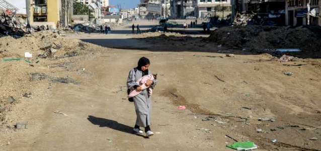 Salma, a 29-year-old, carries her infant while walking on Rashid Street, west of Gaza City