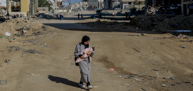 Salma, a 29-year-old, carries her infant while walking on Rashid Street, west of Gaza City, on 11 January 2024.